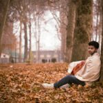 A man wrapped in a shawl sits among fallen autumn leaves in a serene park in Srinagar, India.