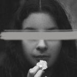 Striking black and white portrait featuring a woman with her eyes obscured, holding an object.